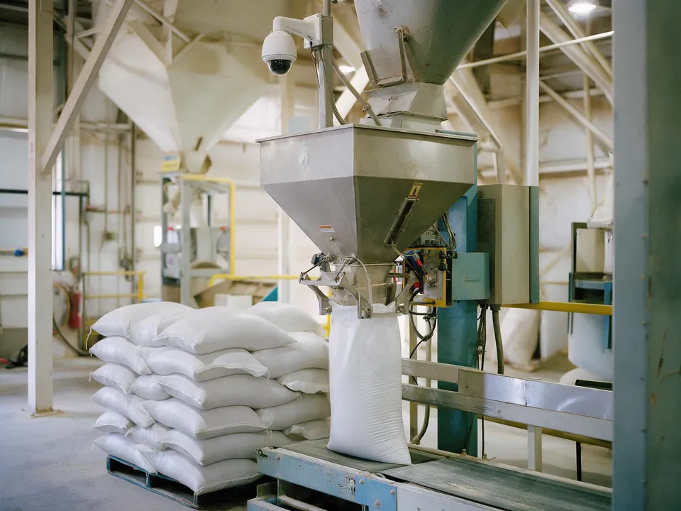 Bagged feed stacked on pallets beside a bagging machine in a feed mill