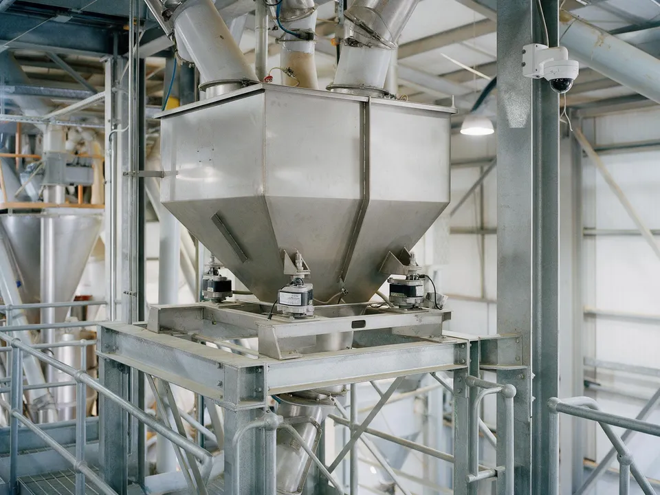 Stainless steel weigh hoppers on a steel frame above a mixer in a feed mill